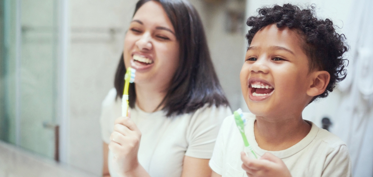child and mother brushing teeth together and laughing